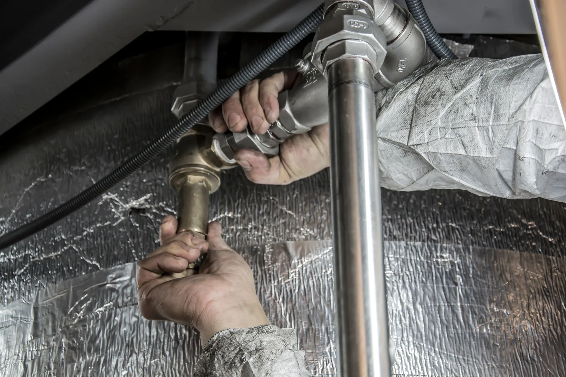 Plumber tightening a chrome supply fitting below a stainless sink